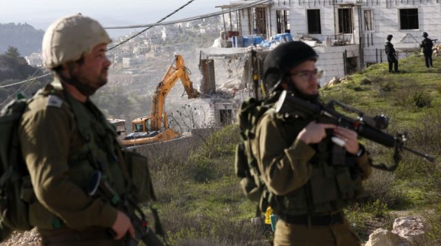Israeli soldiers and border police stand guard as Israeli hydraulic shovels demolish a Palestinian building near road 35.