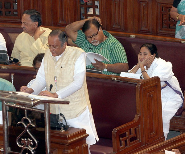 WB Finance Minister Amit Mitra delivering the 2015 budget speech. WB CM Mamata Banerjee and Education Minister Partha Chatterjee, sitting at the bench behind him.