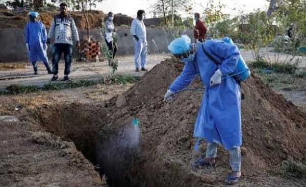 Health worker in protective gear spraying disinfectant inside the grave.